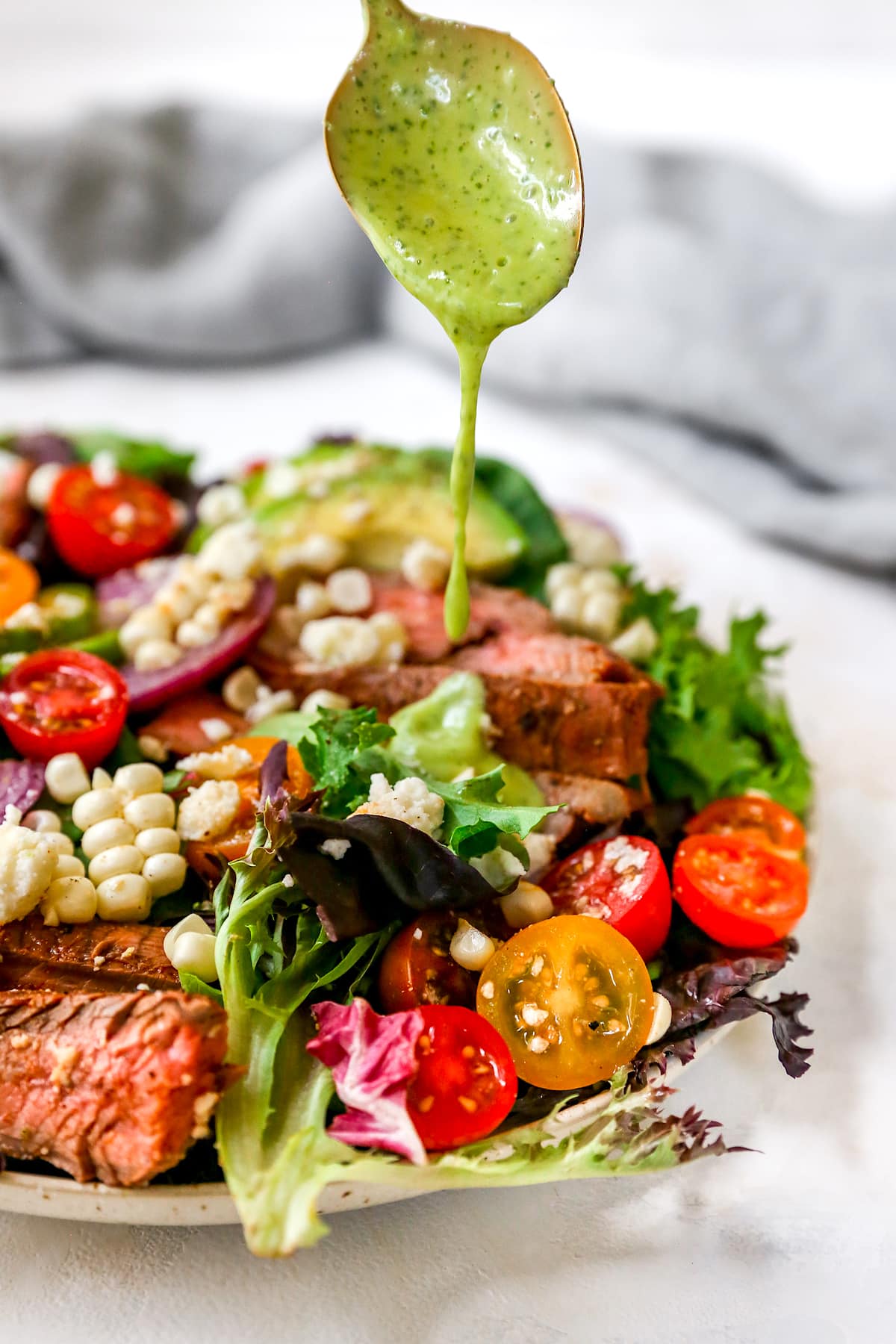 Drizzling creamy cilantro lime dressing over steak salad with spoon.