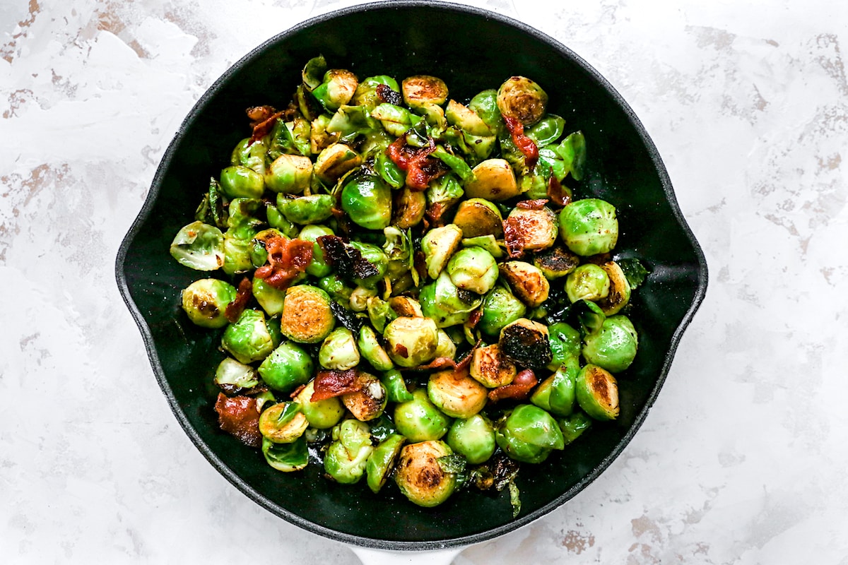 brussels sprouts with bacon cooking in cast iron skillet. 