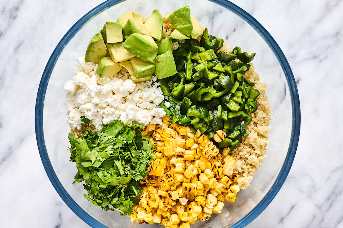 quinoa, corn, poblano pepper, avocado, cilantro, and cotija cheese in glass mixing bowl. 