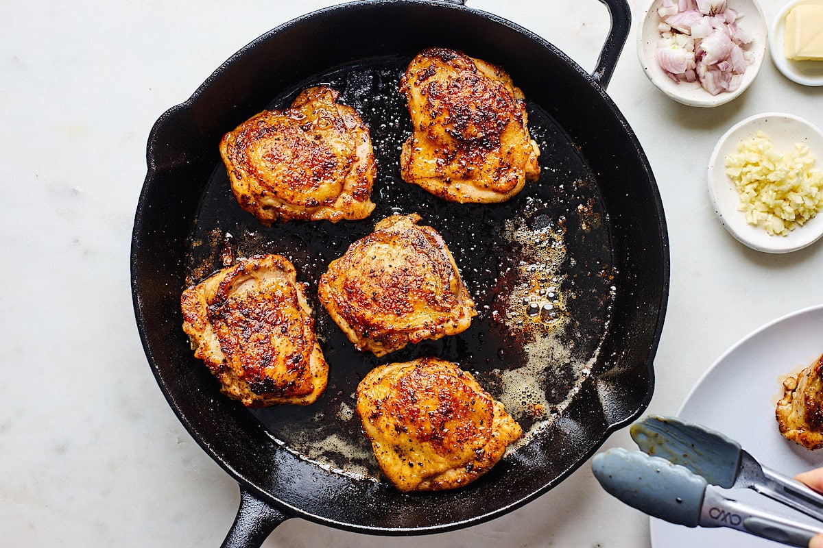 crispy chicken thighs cooking in cast iron skillet. 