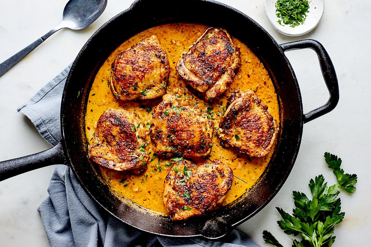 chicken thighs simmering in garlic cream sauce in cast iron skillet. 