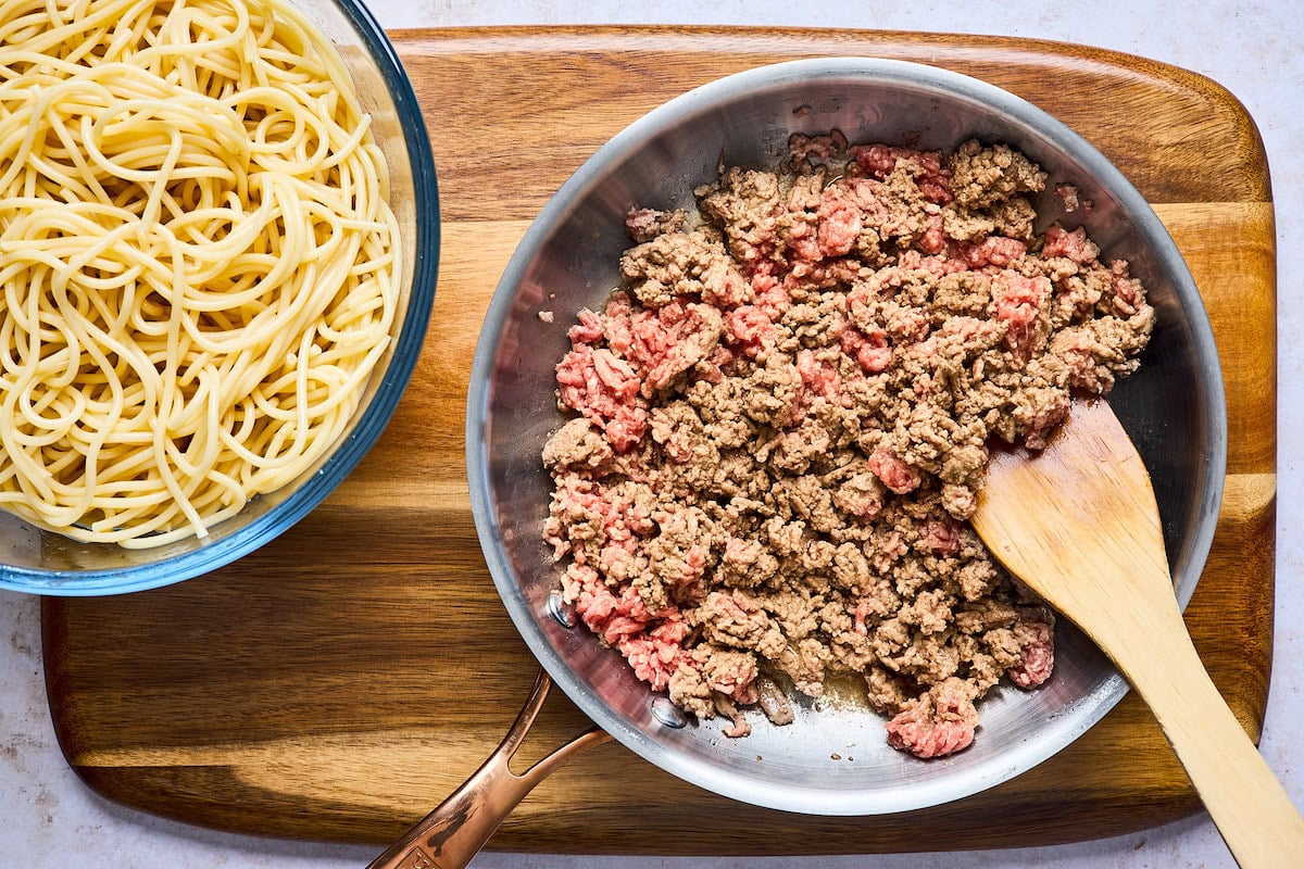 cooked spaghetti in bowl and ground beef cooking in skillet to make baked spaghetti. 