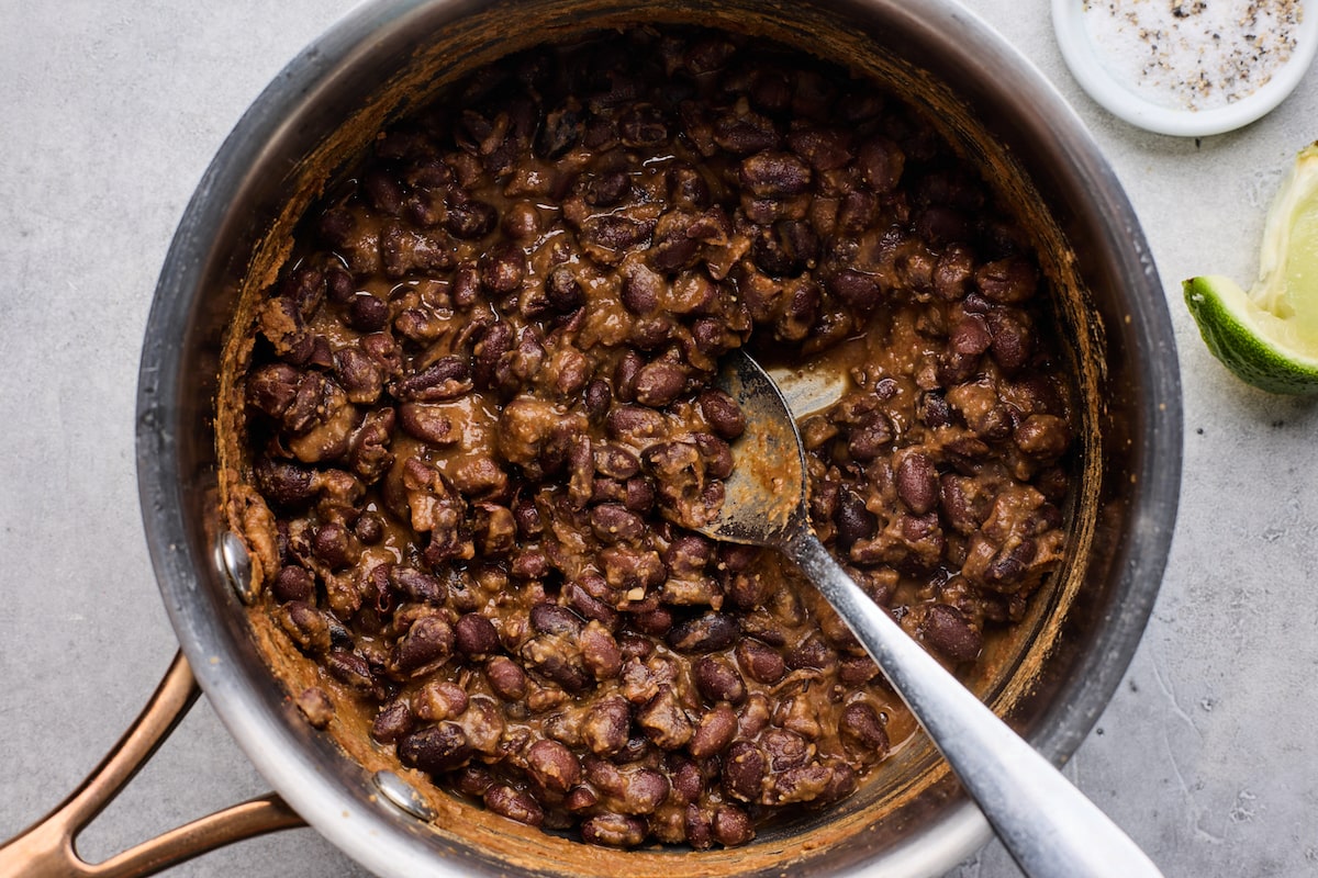 mashed black beans in pot with spoon. 