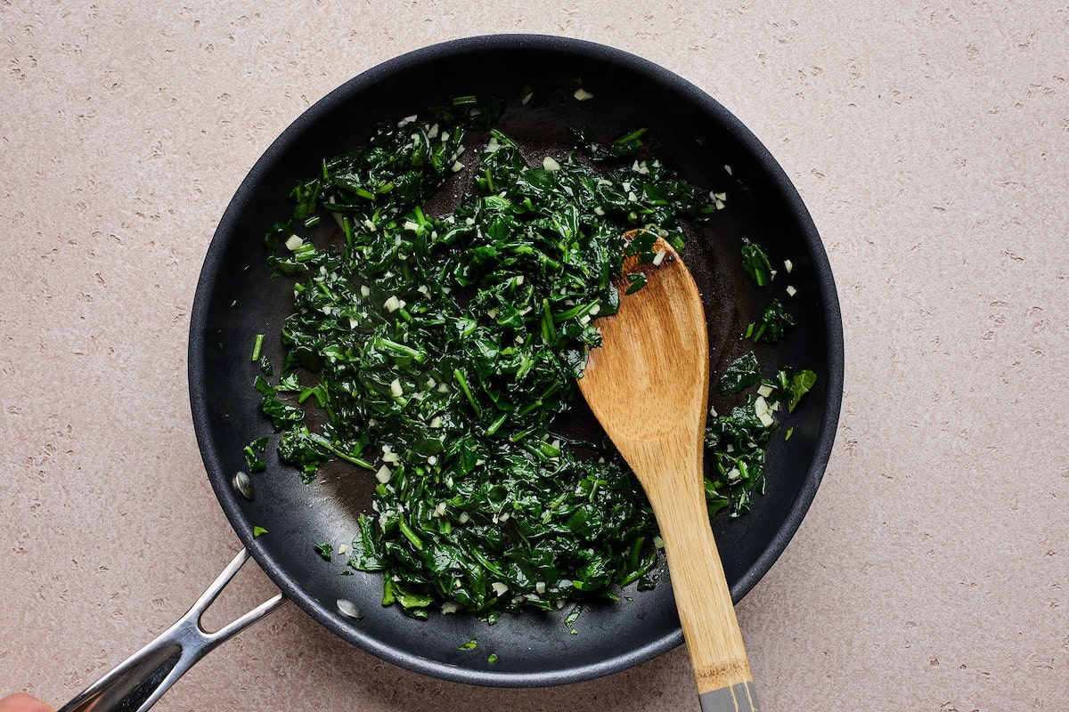 sautéed spinach with garlic in skillet with wooden spoon. 