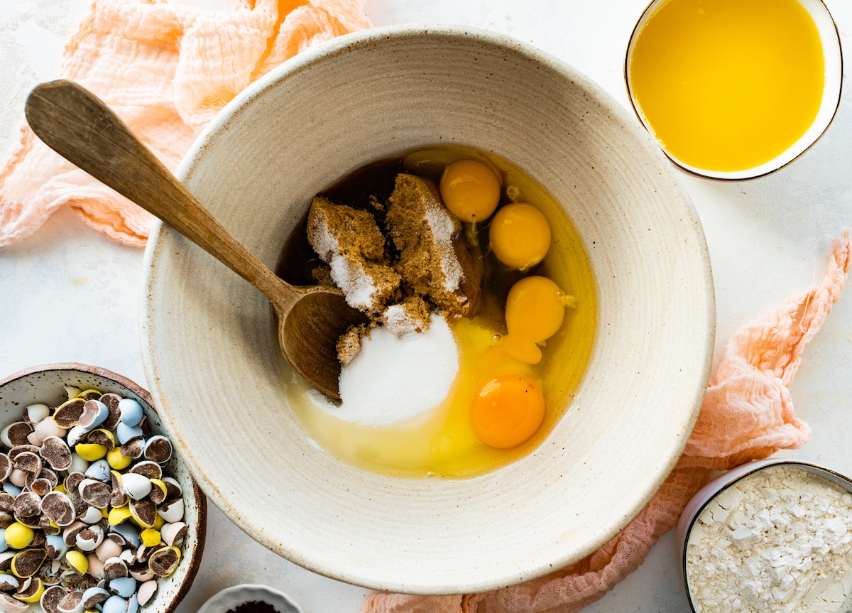 eggs and sugars in mixing bowl with wooden spoon. 