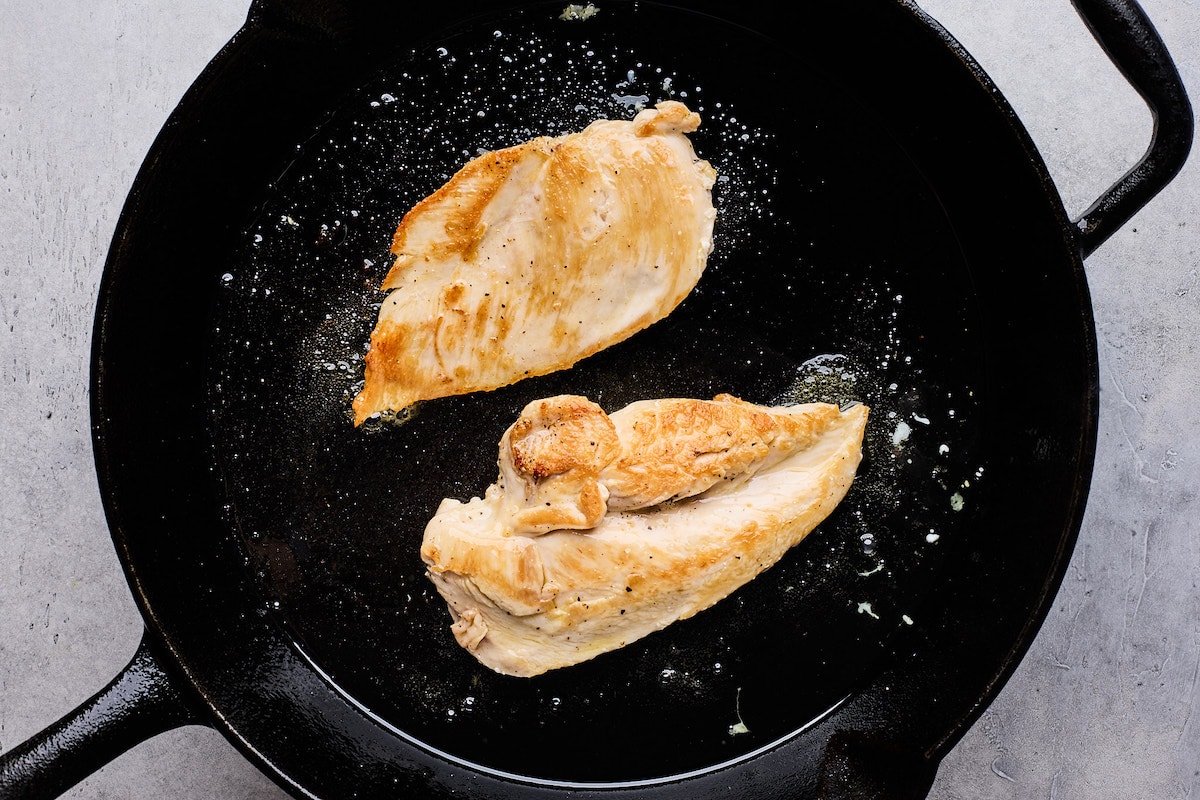 chicken breasts cooking in cast iron skillet. 