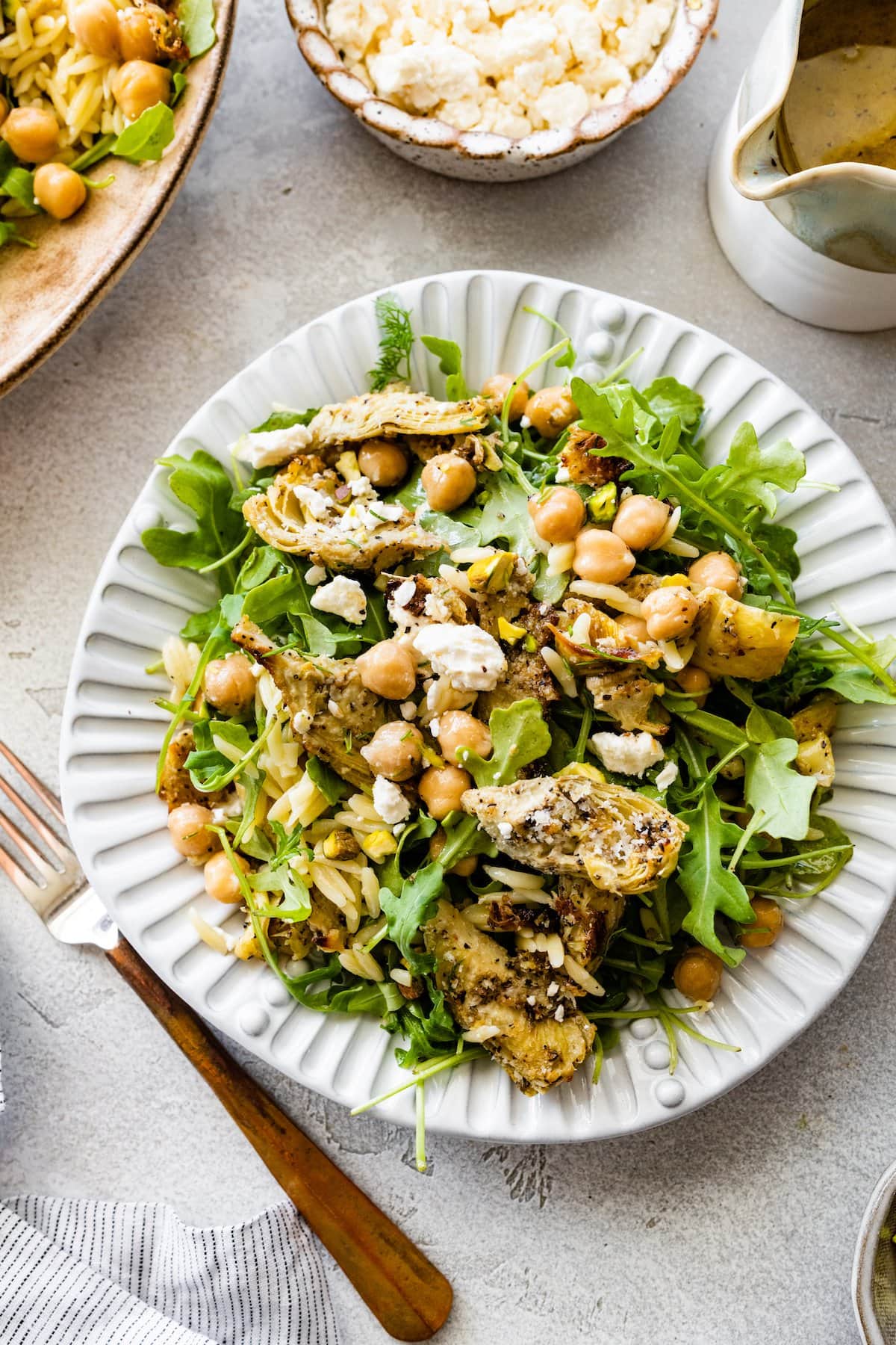 roasted artichoke chickpea orzo salad with arugula and feta cheese on plate with fork. 