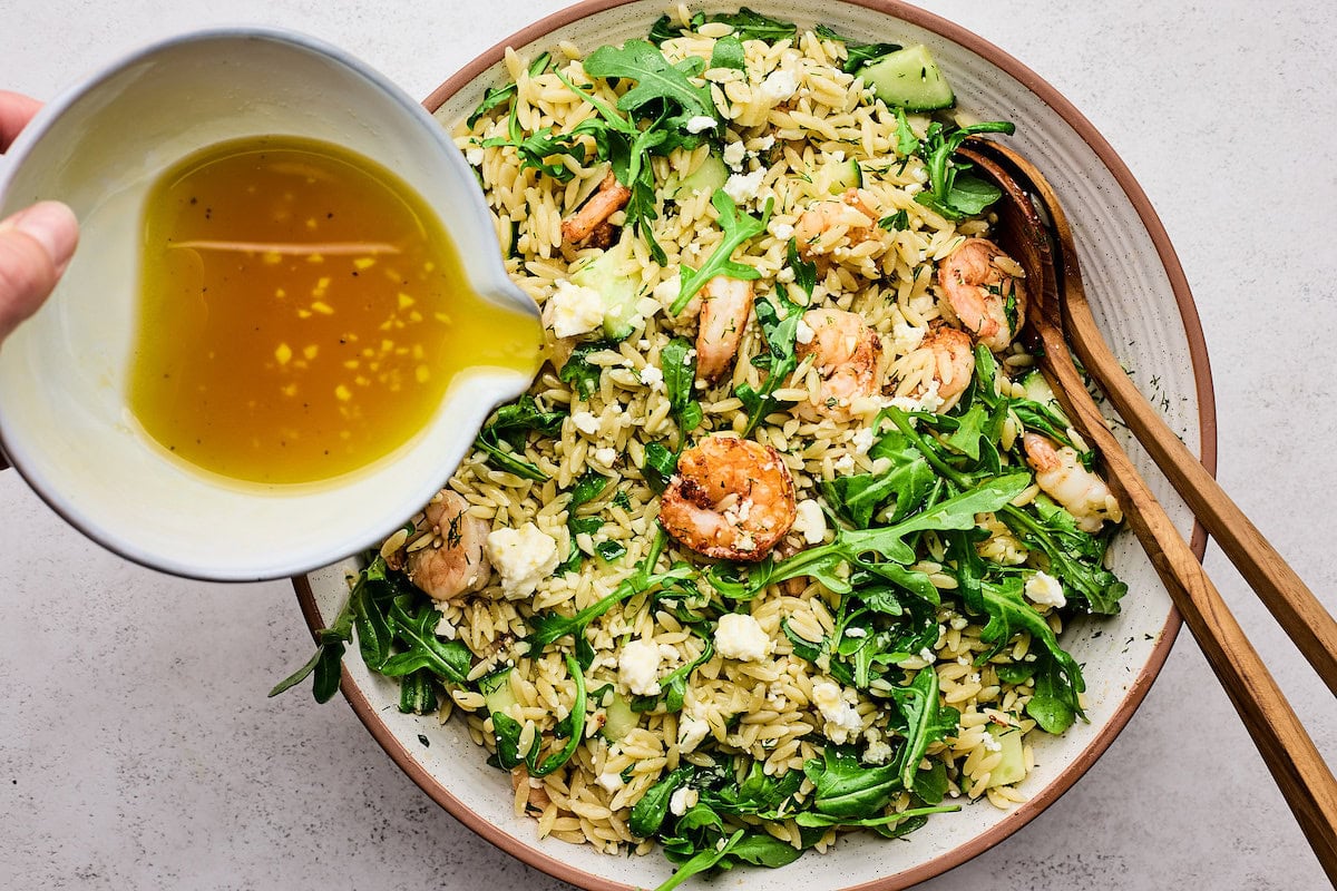 dressing being poured over shrimp orzo salad. 