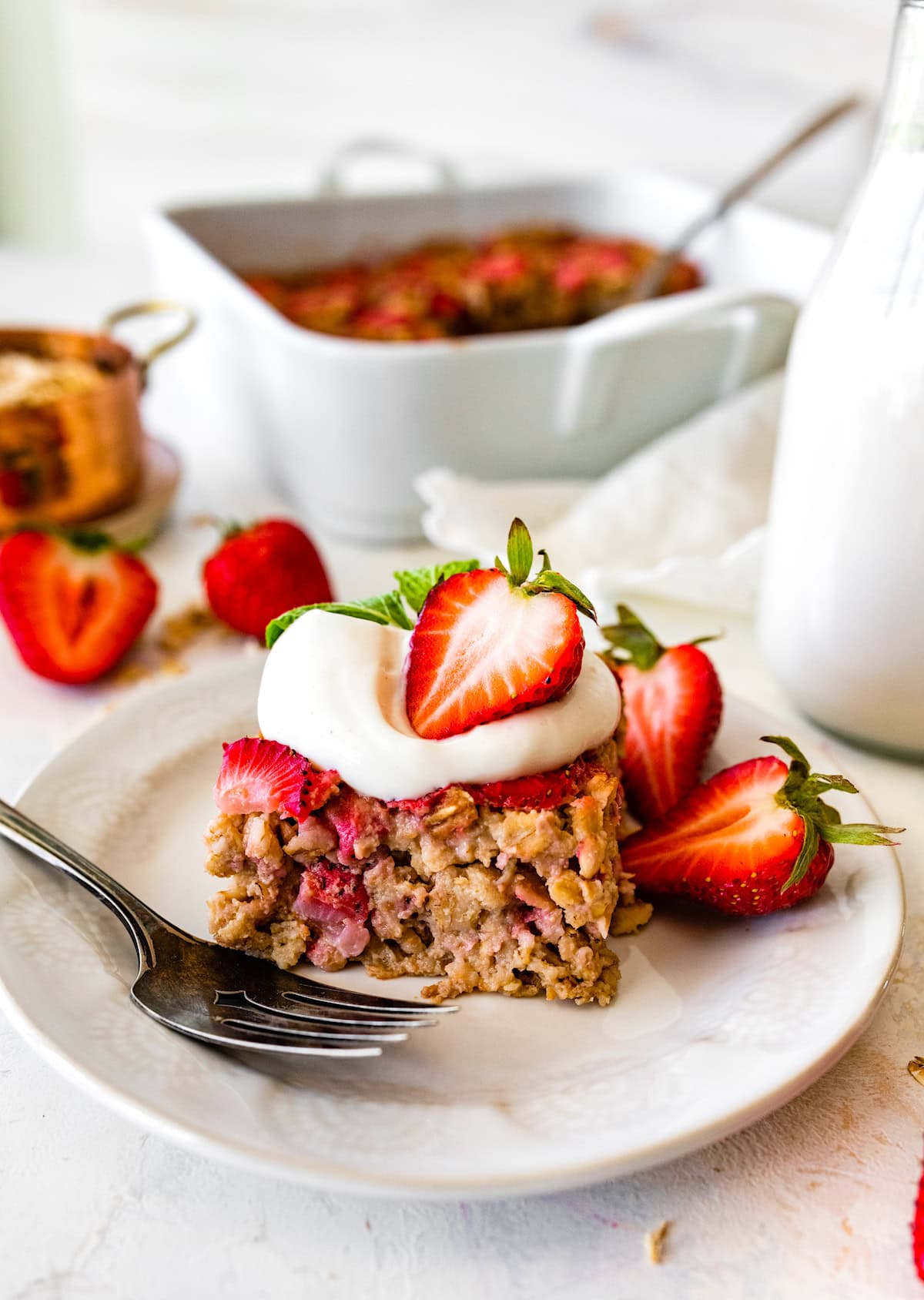 piece of strawberry baked oatmeal on plate with a dollop of yogurt, fresh strawberries, and a fork. 