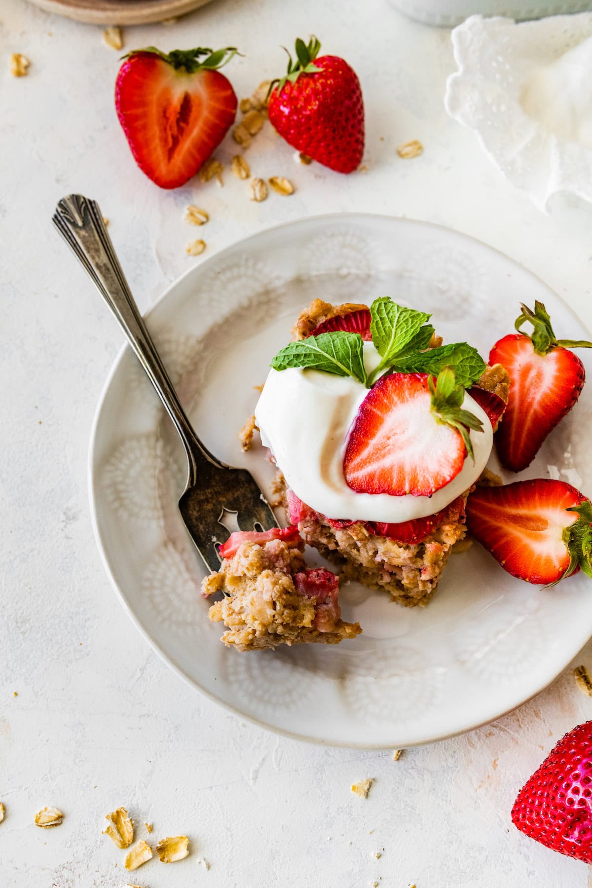 piece of strawberry baked oatmeal with yogurt and fresh strawberries on plate with fork. 
