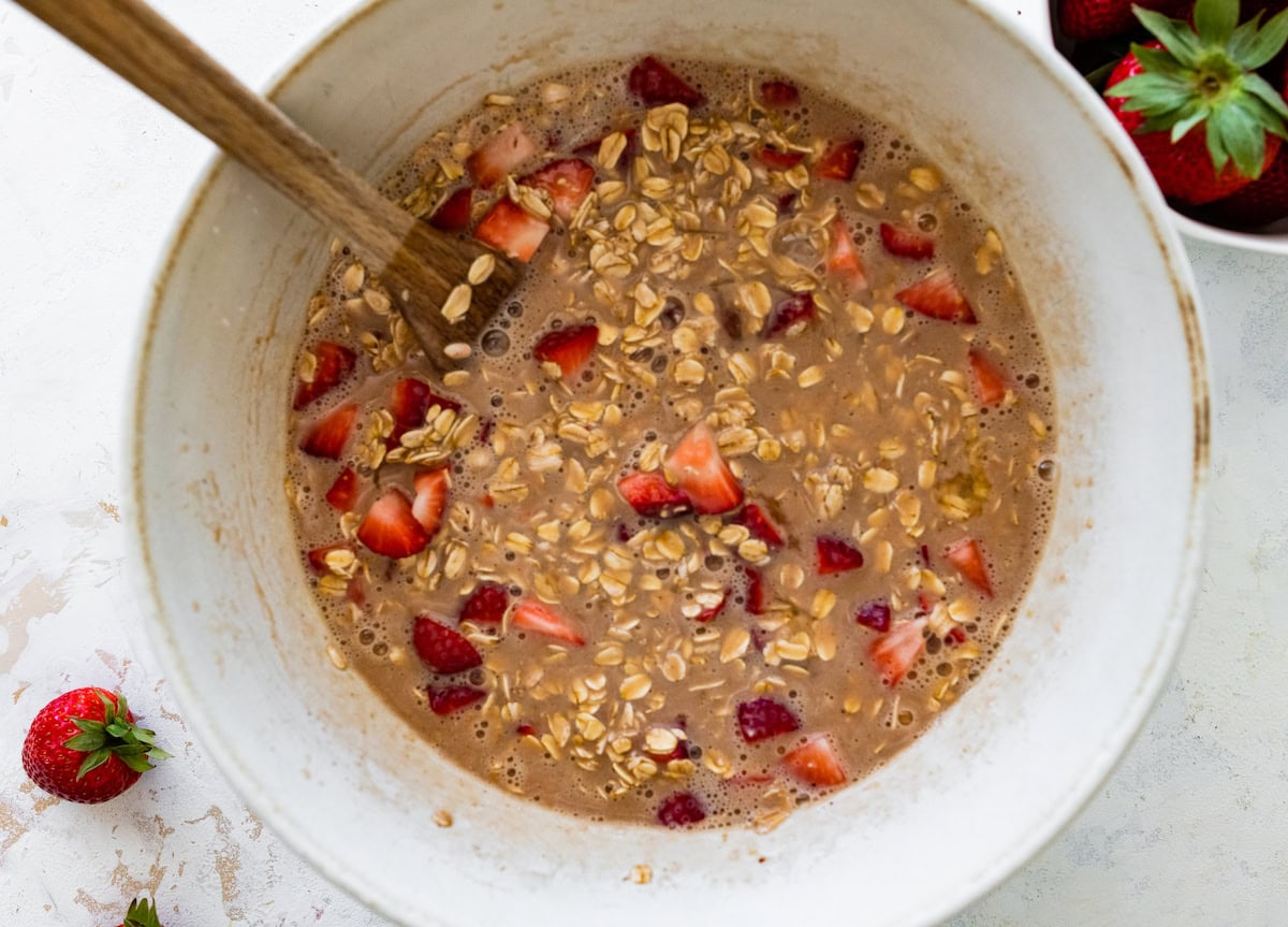 strawberry baked oatmeal mixture in mixing bowl with wooden spoon. 