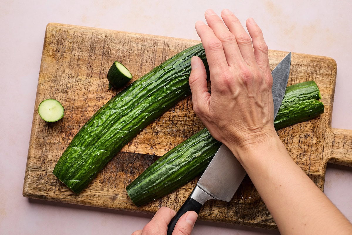 cucumbers on cutting board being smashed with a knife. 