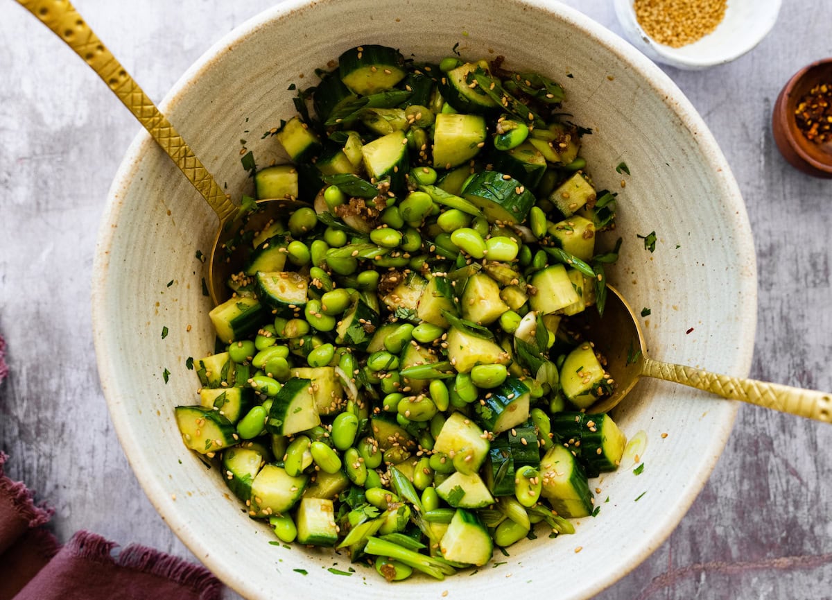 cucumber edamame salad in bowl with salad servers. 