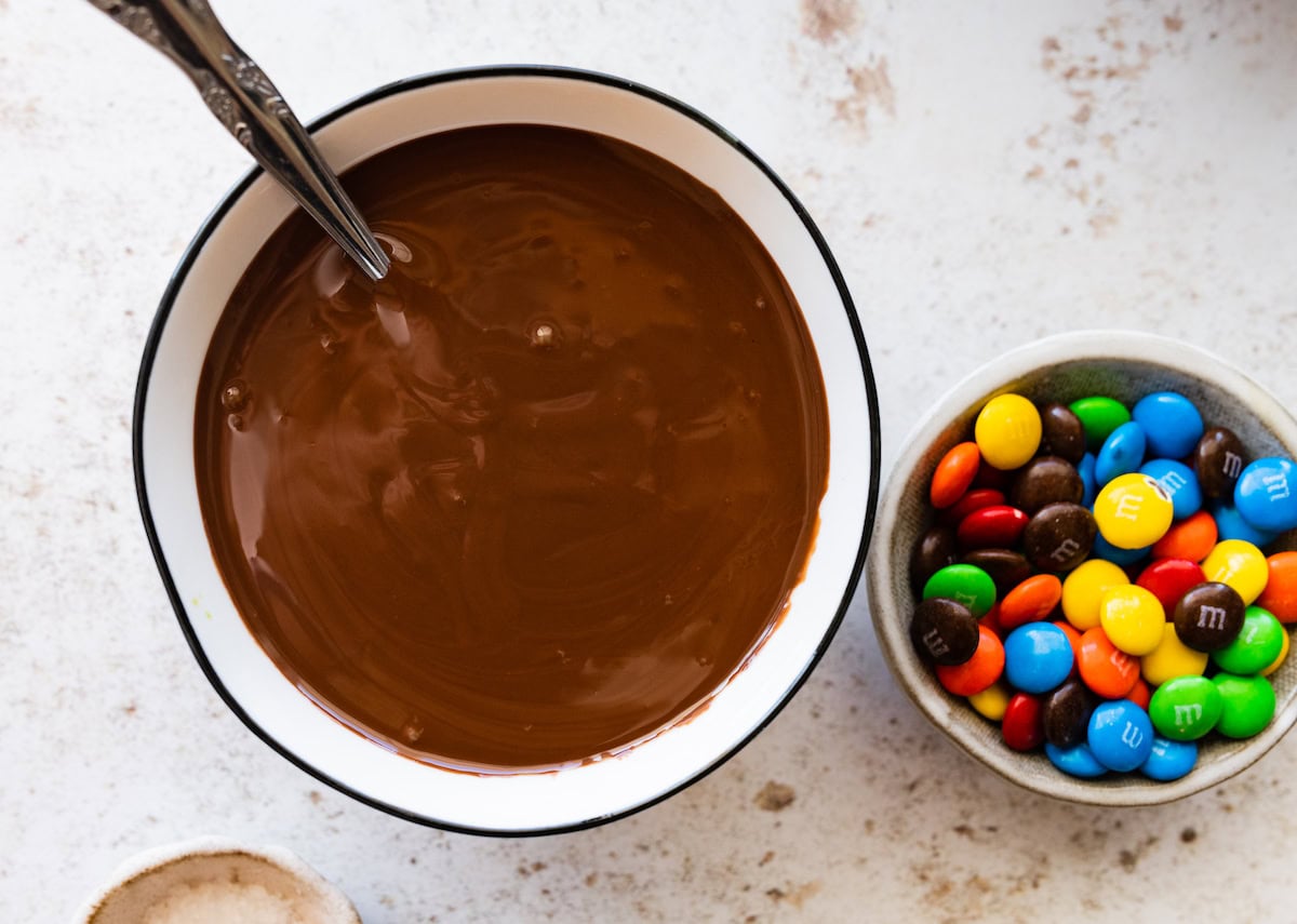 melted chocolate in bowl with spoon and small bowl of M&M's. 
