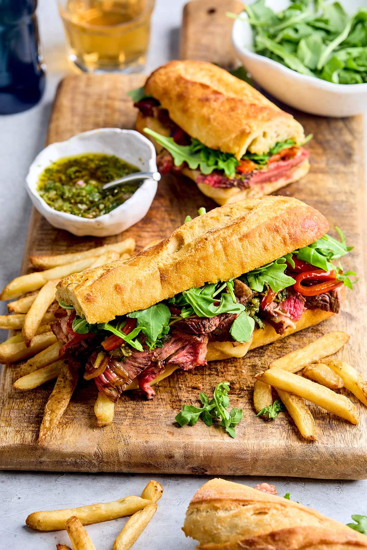 steak sandwich with peppers, onion, provolone cheese, chimichurri, arugula on baguette with fries. 