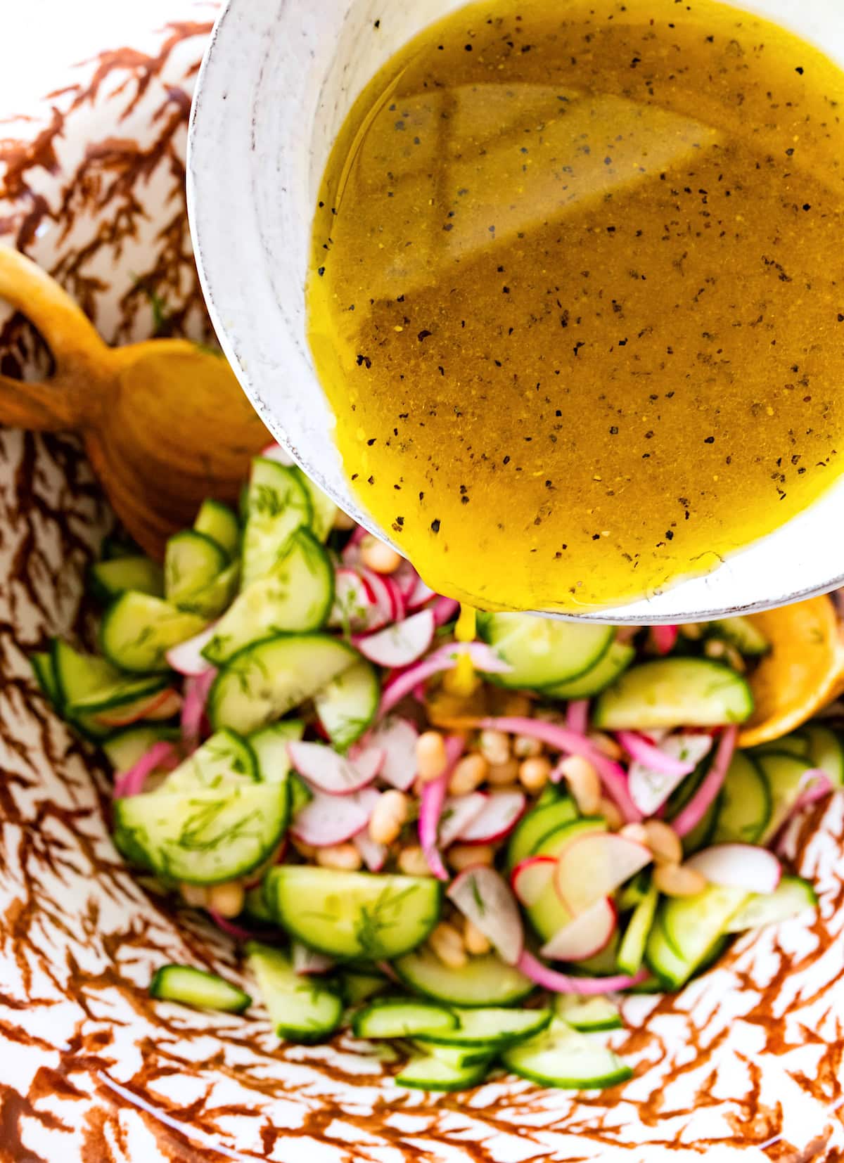 dressing being poured over white bean cucumber salad. 