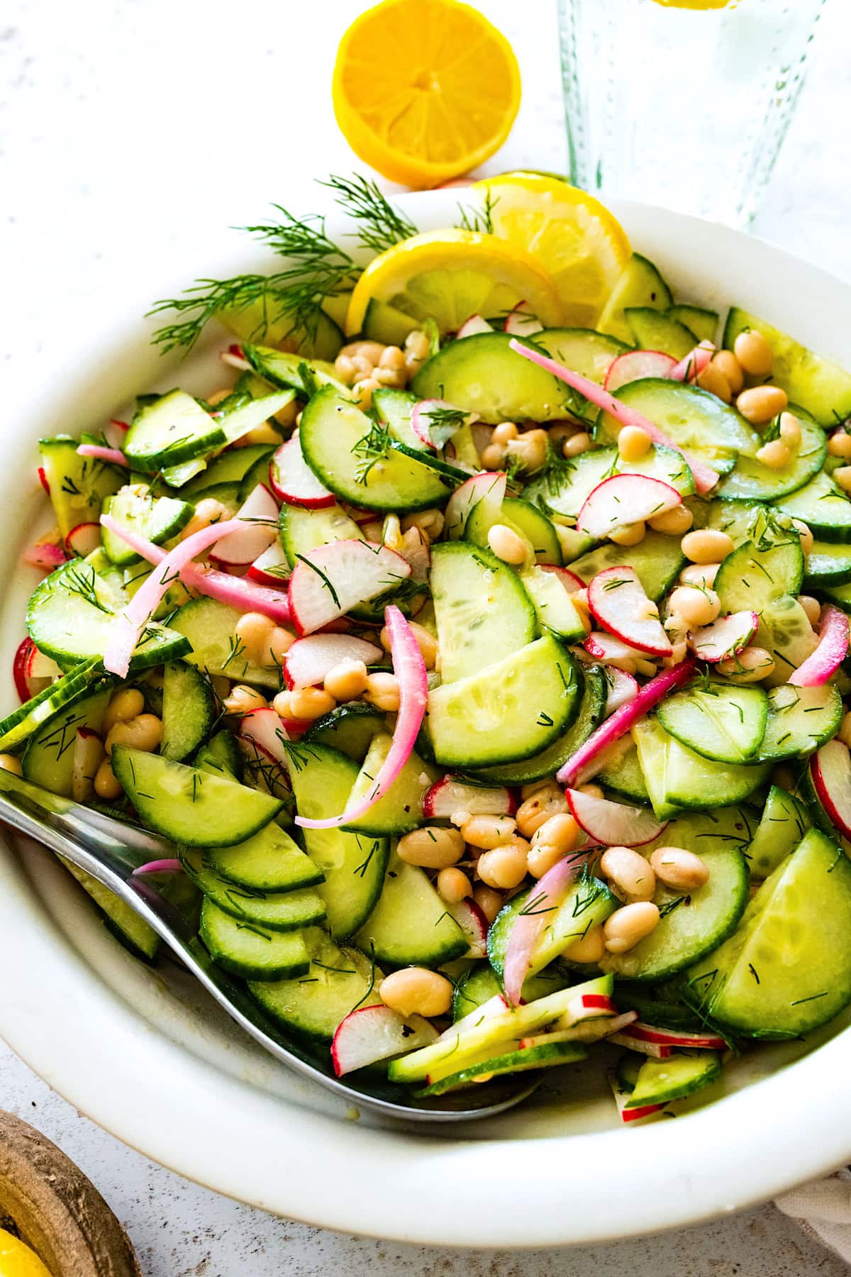white bean cucumber salad with red onion, radishes, dill, and lemon in serving bowl with spoon. 