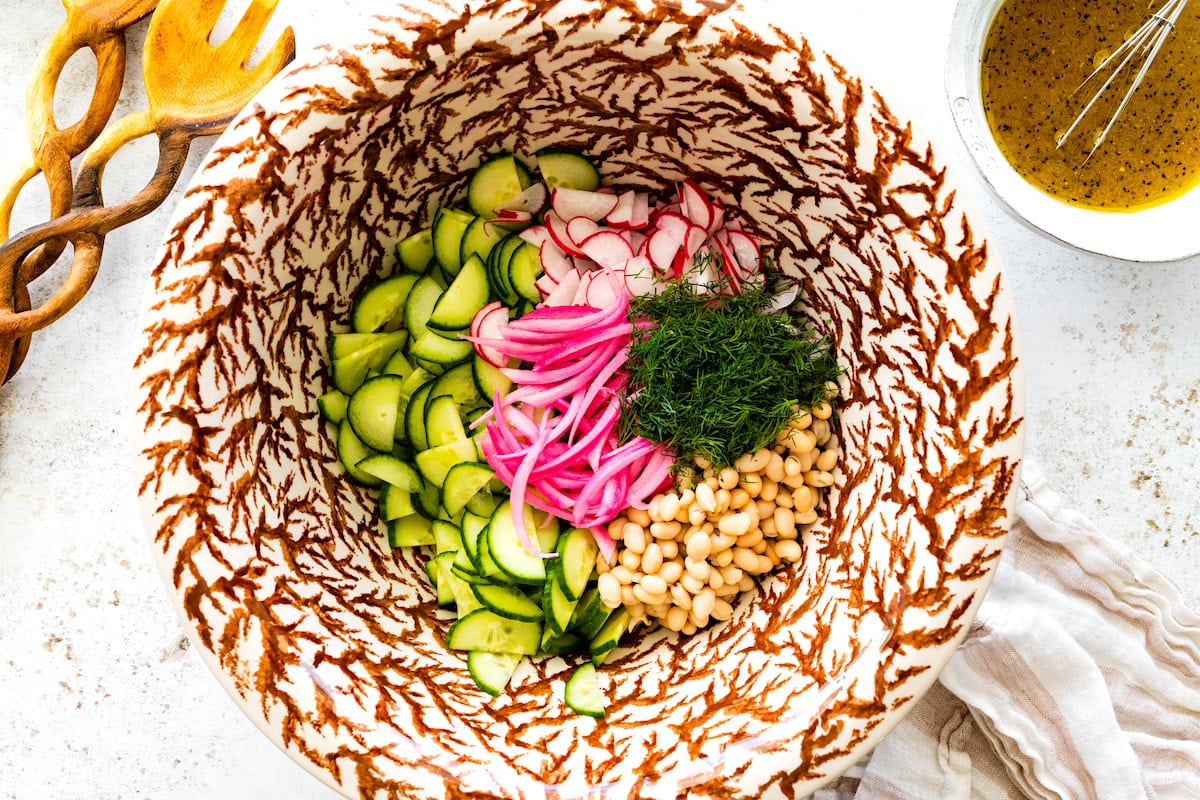 white beans, cucumber, red onion, radish, and dill in bowl to make white bean cucumber salad. 