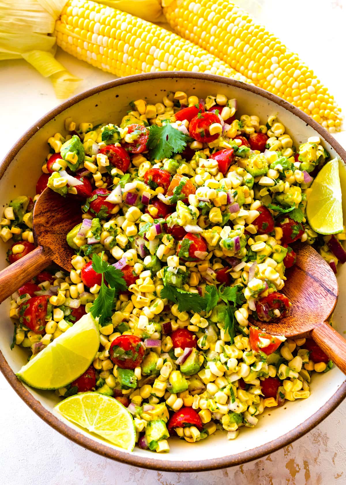 avocado corn salad in serving bowl with salad servers. 