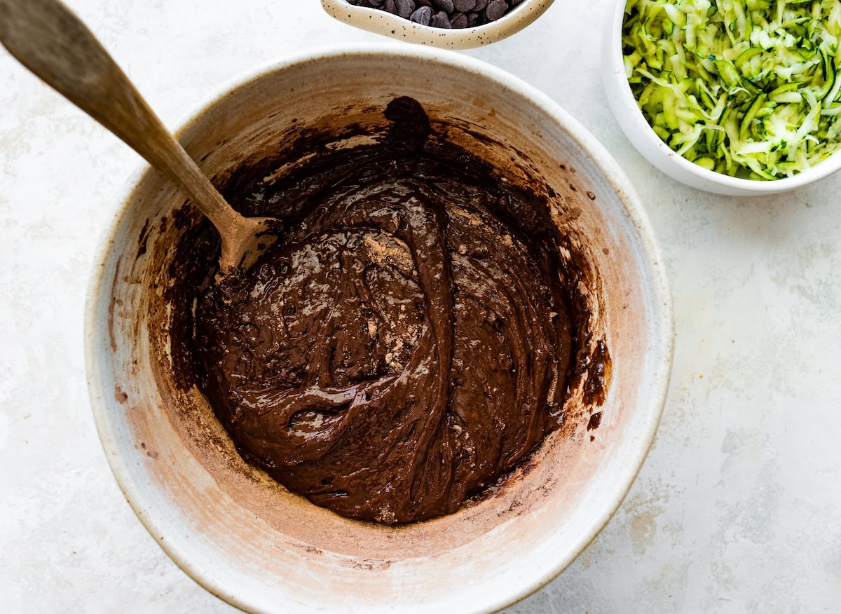 chocolate zucchini cake batter in mixing bowl with wooden spoon. 