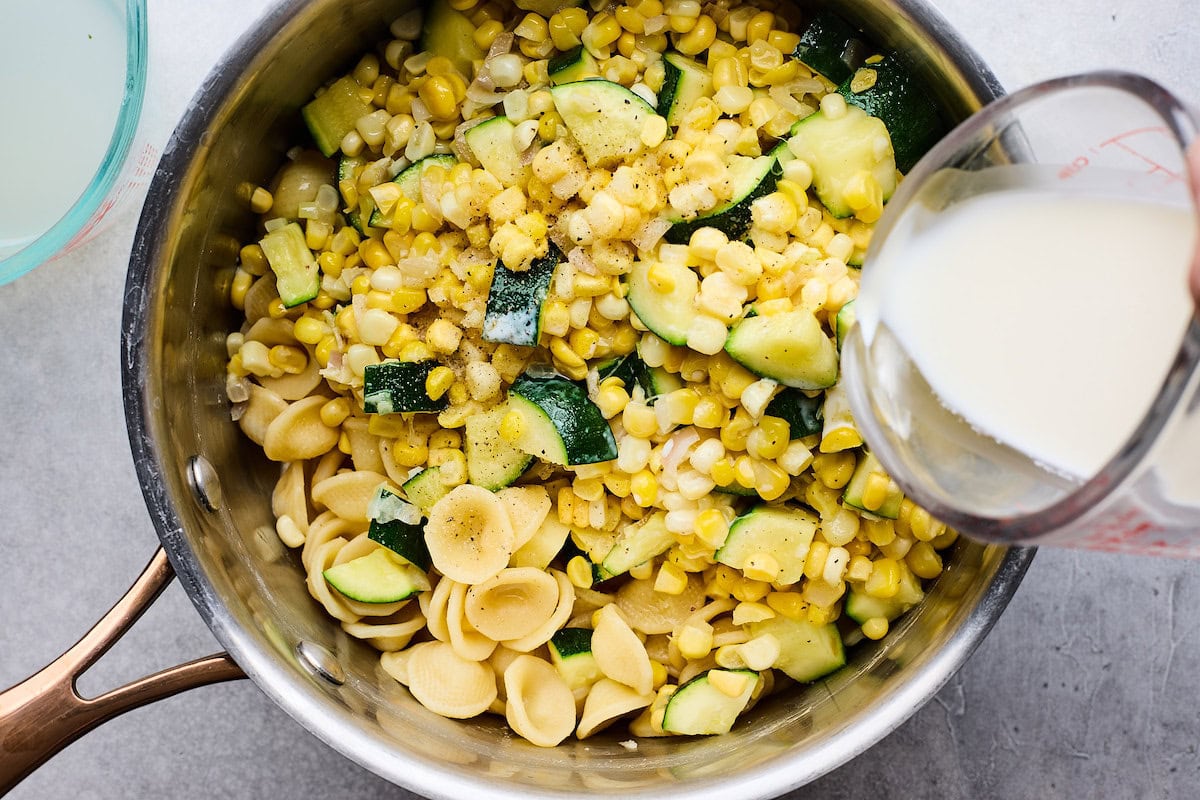 heavy cream being poured over zucchini corn pasta. 