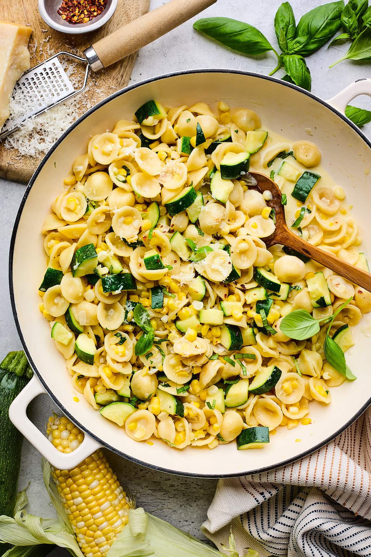 creamy zucchini corn pasta in skillet with wooden spoon. 