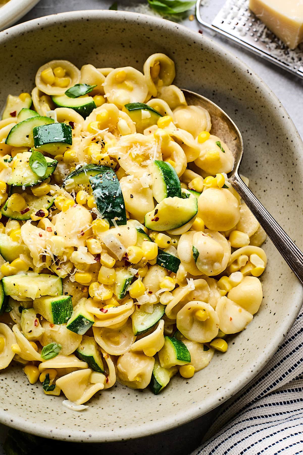 close up of creamy zucchini corn pasta in bowl with spoon. 