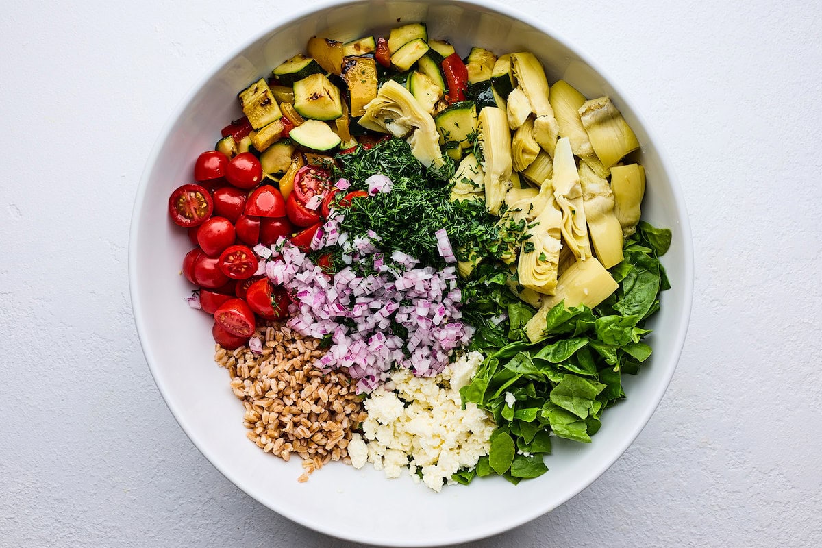 grilled zucchini, peppers, artichokes, spinach, feta, farro, red onion, herbs, and tomatoes in serving bowl. 