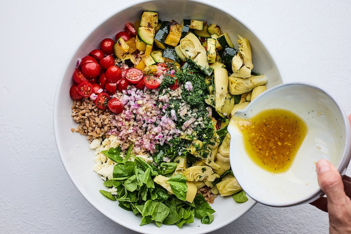 dressing being poured over grilled vegetable farro salad. 