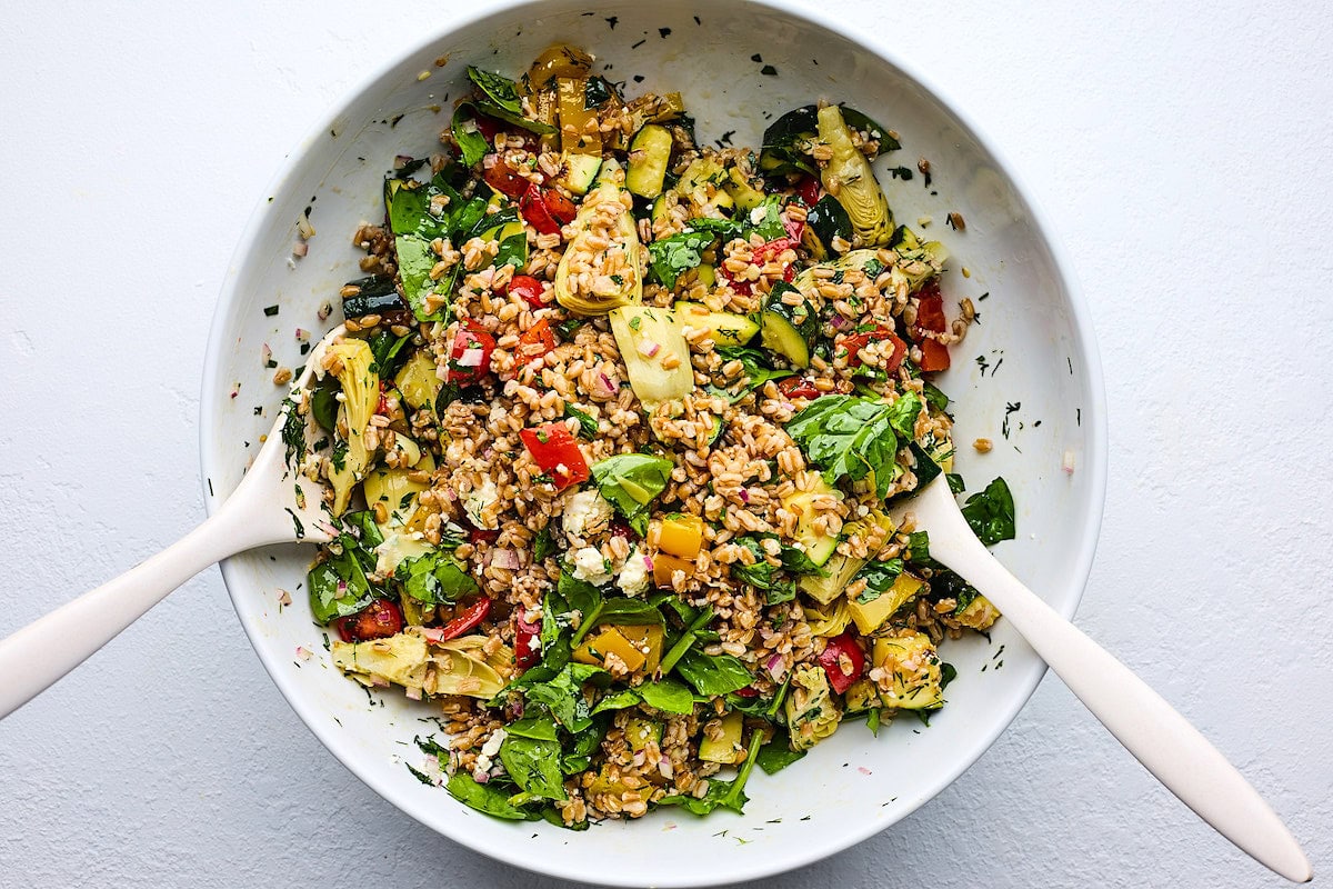 grilled vegetable farro salad in serving bowl with salad servers. 