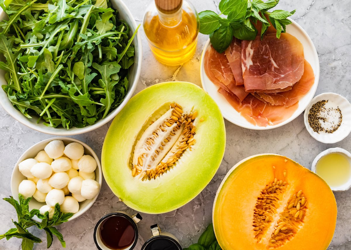 arugula, olive oil, basil, prosciutto, fresh mozzarella, and melons to make melon and prosciutto salad. 