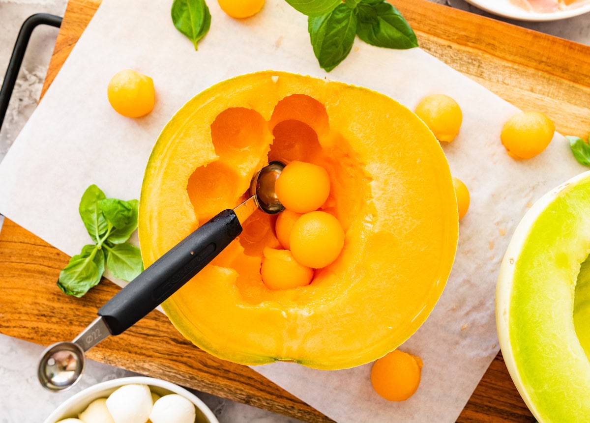 melon being scooped with a melon baller on cutting board. 