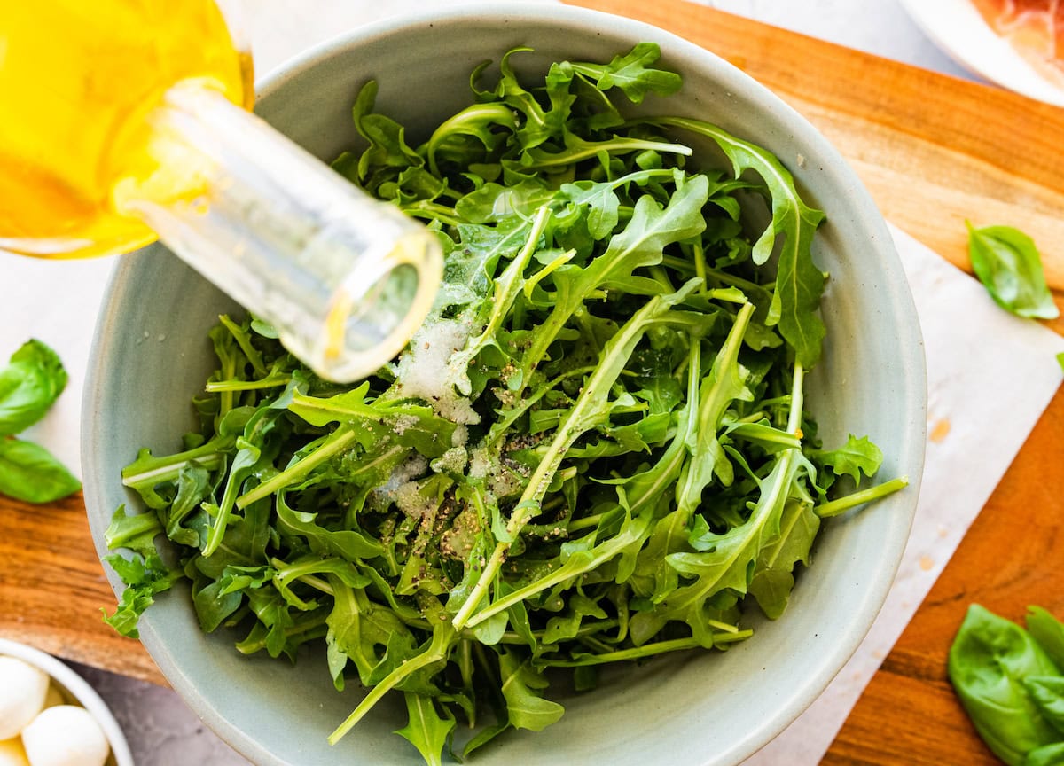 olive oil being drizzled over arugula in a bowl. 