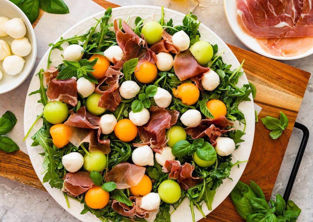 arugula on platter with melon balls, fresh mozzarella, and prosciutto. 