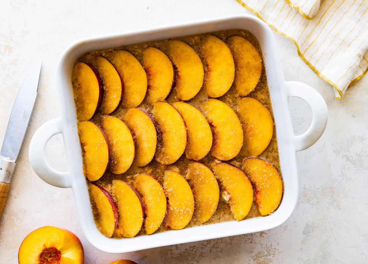 unbaked peach oatmeal in white pan with fresh peach slices. 