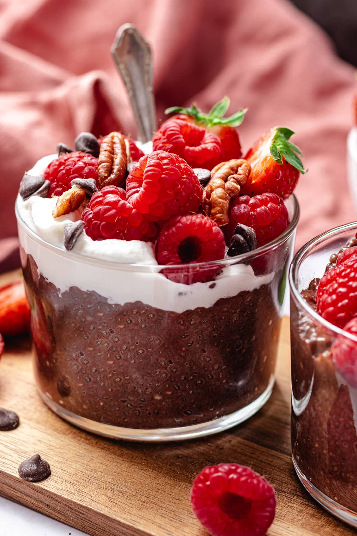 chocolate chia pudding with whipped cream, raspberries, pecans, and chocolate chips in glass jar with spoon.