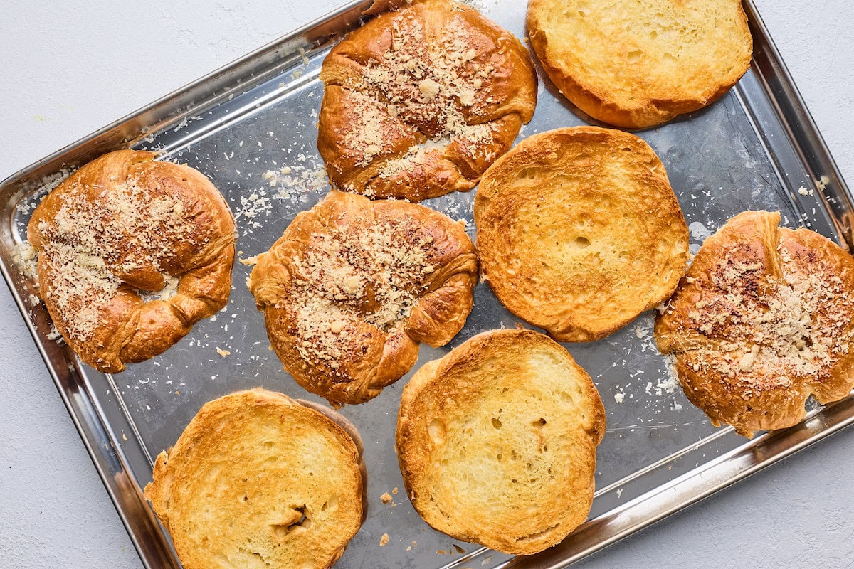 toasted croissants cut in half with parmesan cheese on baking sheet. 