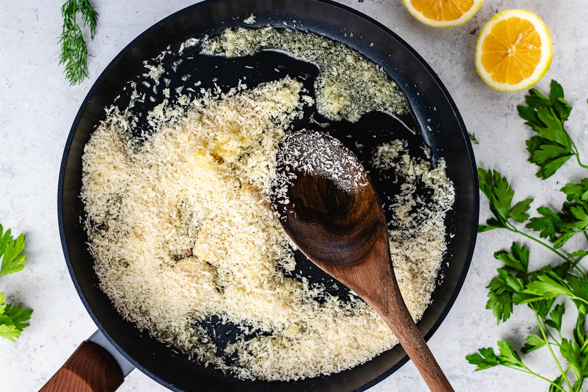 breadcrumbs toasting in skillet with wooden spoon. 