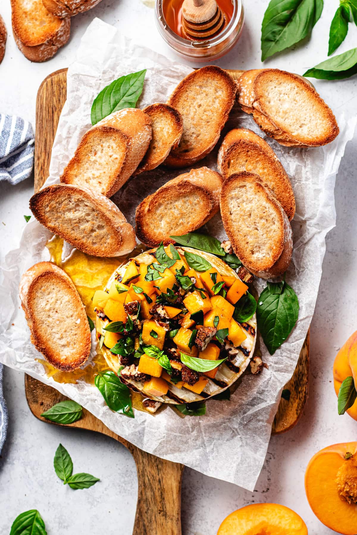 grilled brie with peaches on wood board with crostini. 