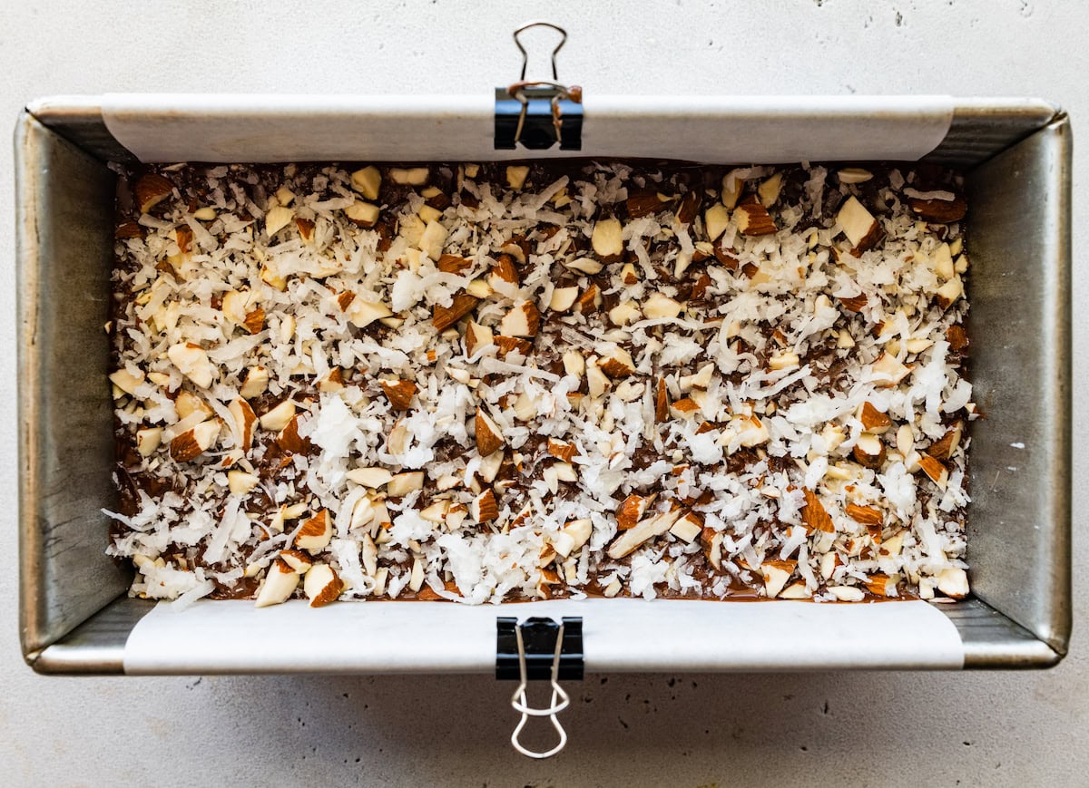 coconut and almonds sprinkled on top of no bake almond joy bars in loaf pan. 