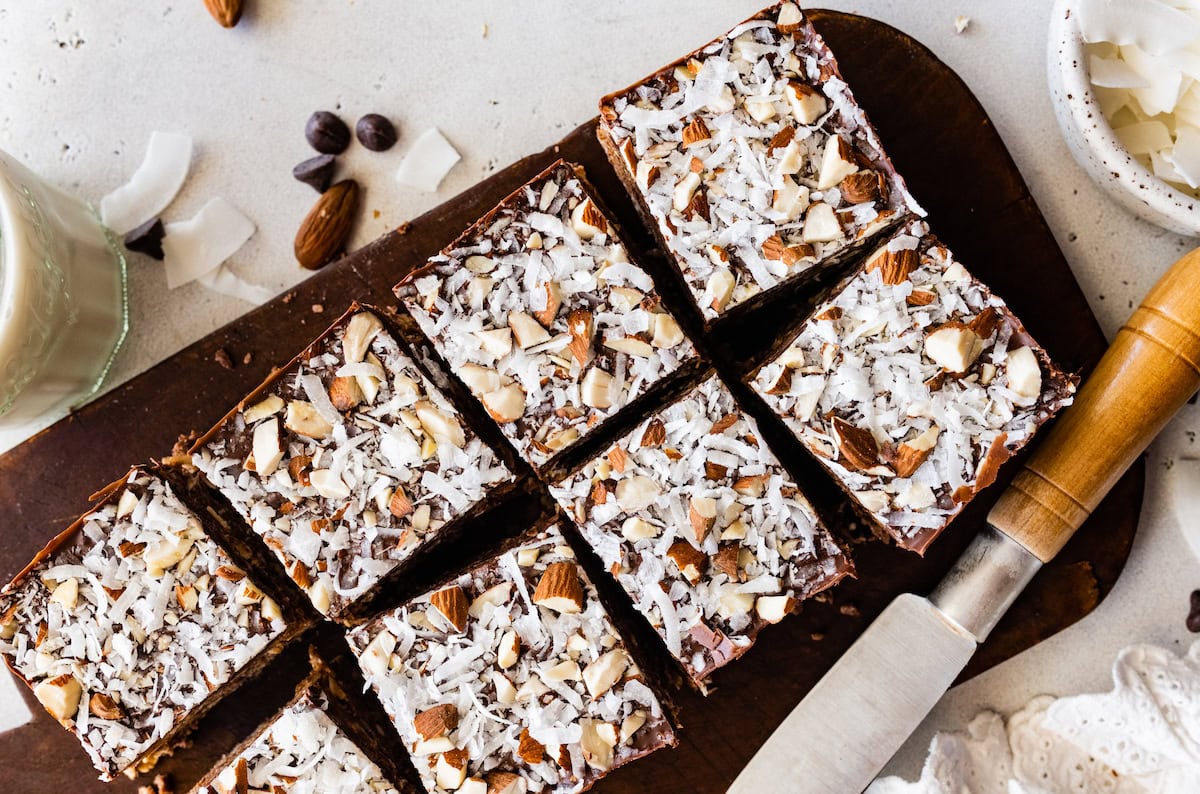 no bake almond joy bars cut into squares on wood cutting board with knife. 