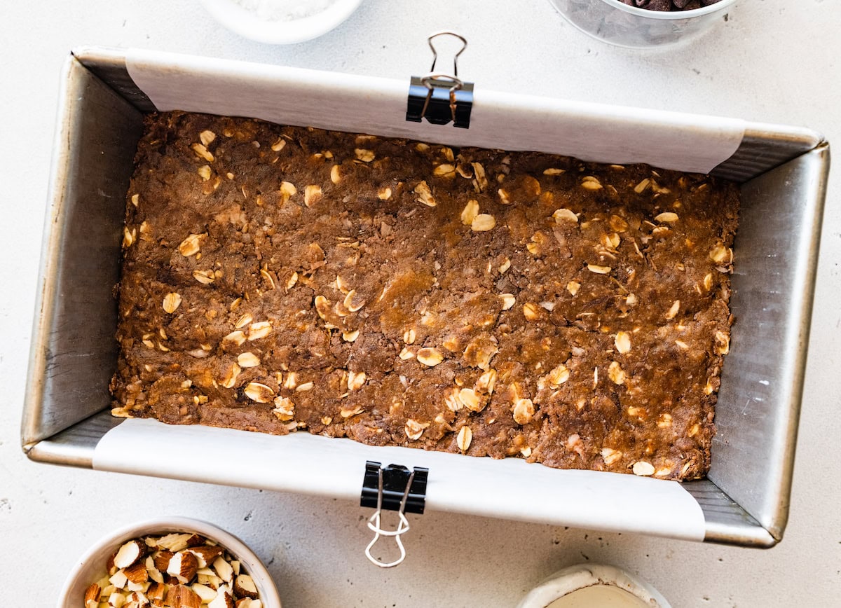 chocolate coconut oat mixture pressed in loaf pan lined with parchment paper to make no bake almond joy bars. 