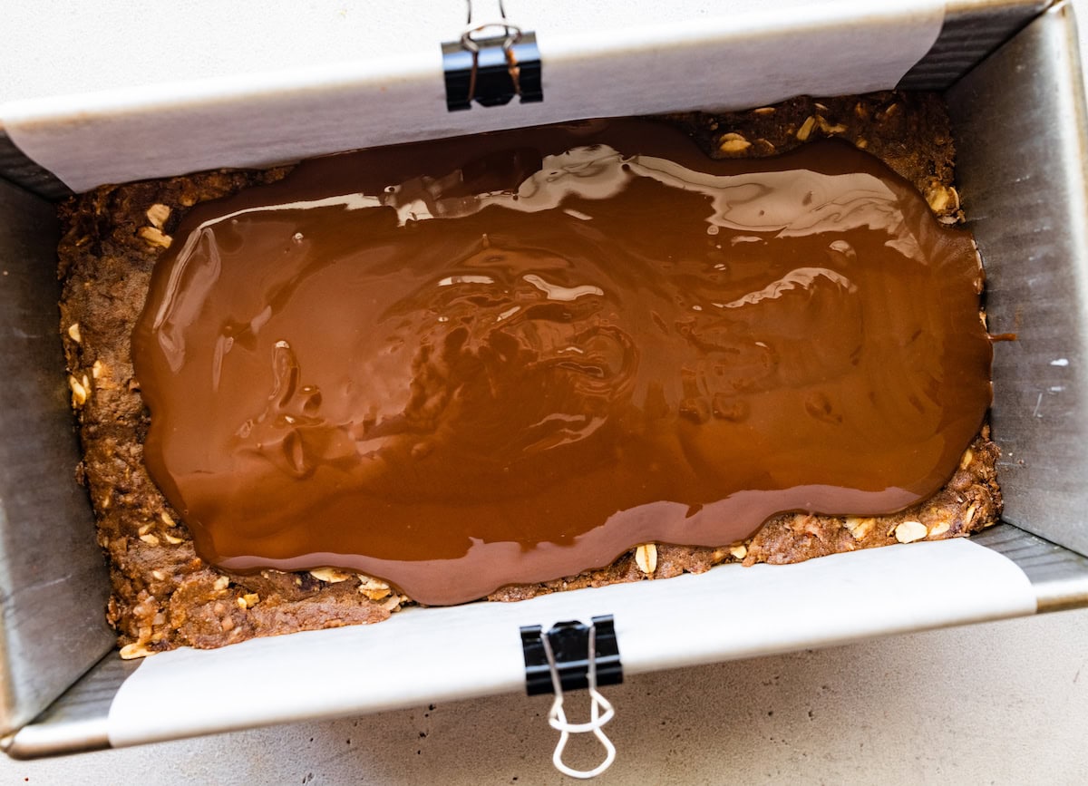 melted chocolate spread on top of no bake almond joy bars in loaf pan. 