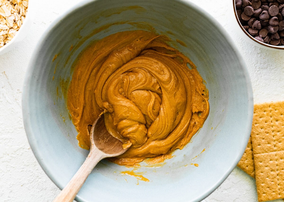 peanut butter mixture being stirred in bowl with wooden spoon. 