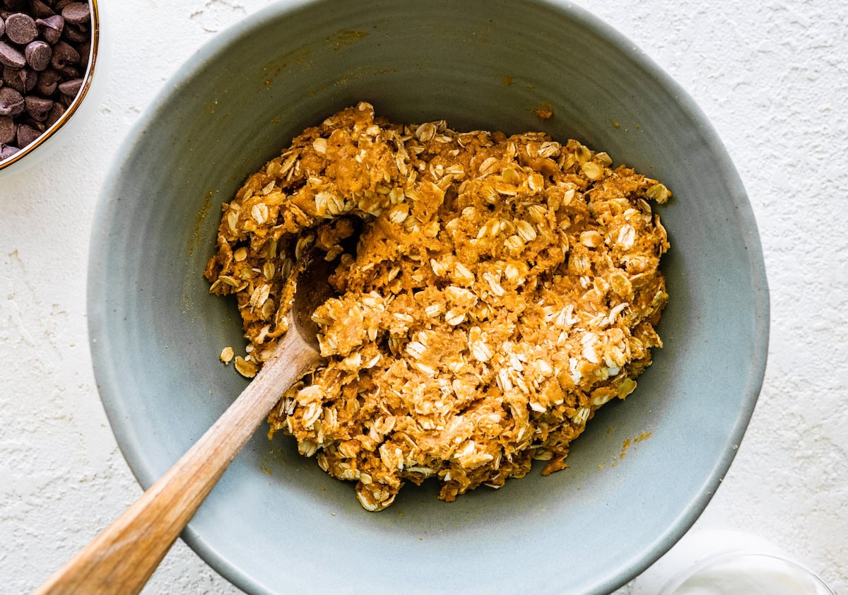 peanut butter, graham cracker, and oat mixture in mixing bowl with wooden spoon. 