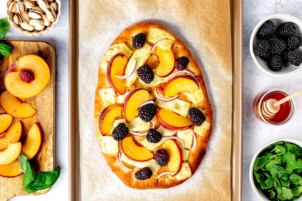 peach flatbread with melted brie, peaches, blackberries, and red onion on baking sheet. 