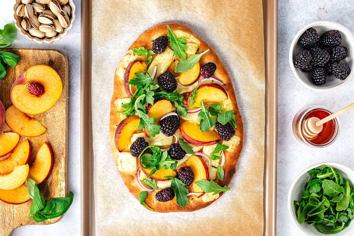 peach brie flatbread with arugula, blackberries, and red onion on baking sheet. 