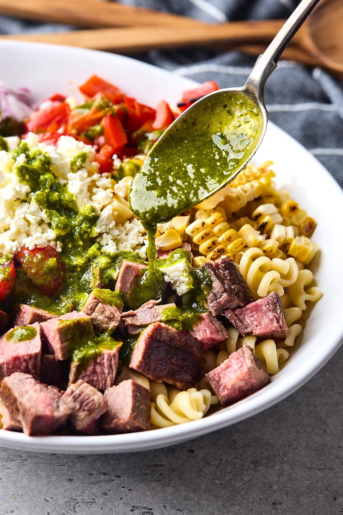 cilantro lime vinaigrette being spooned over steak pasta salad. 