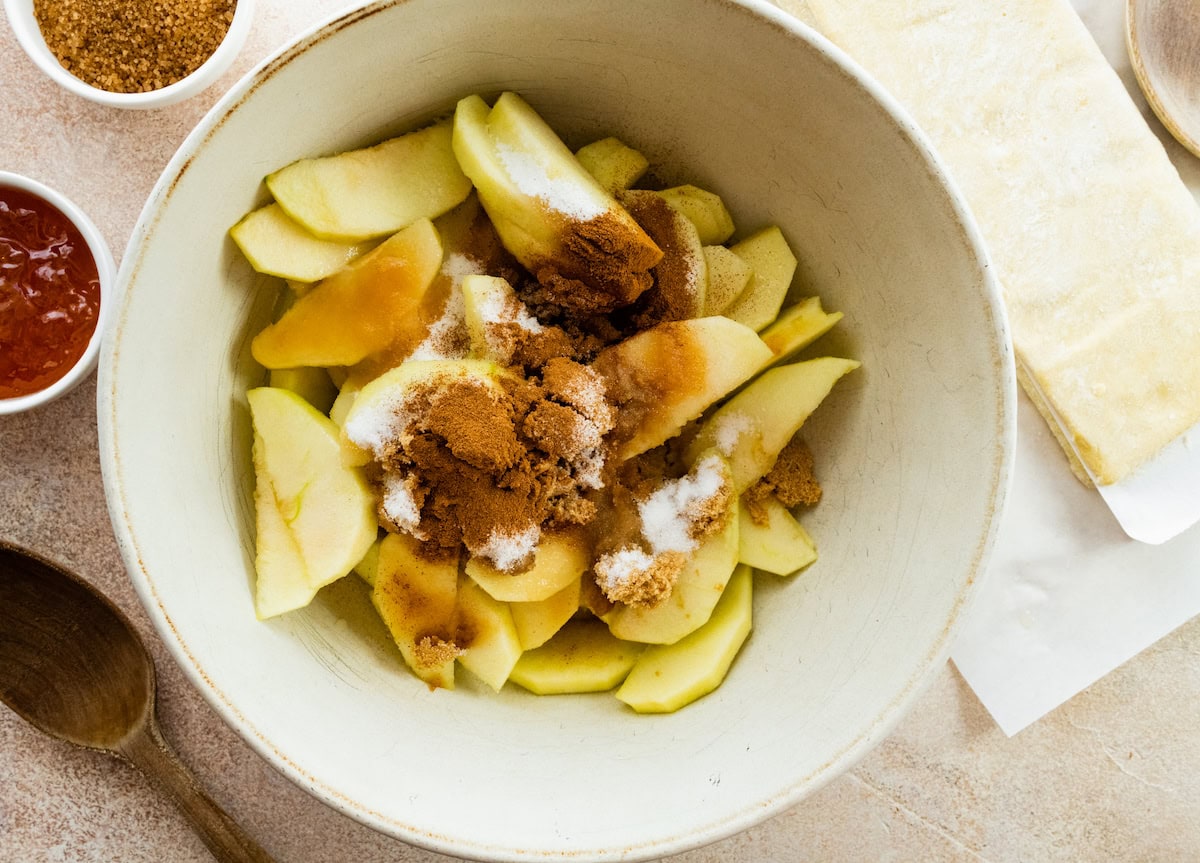 apple slices in bowl with sugar and cinnamon to make puff pastry apple tart. 