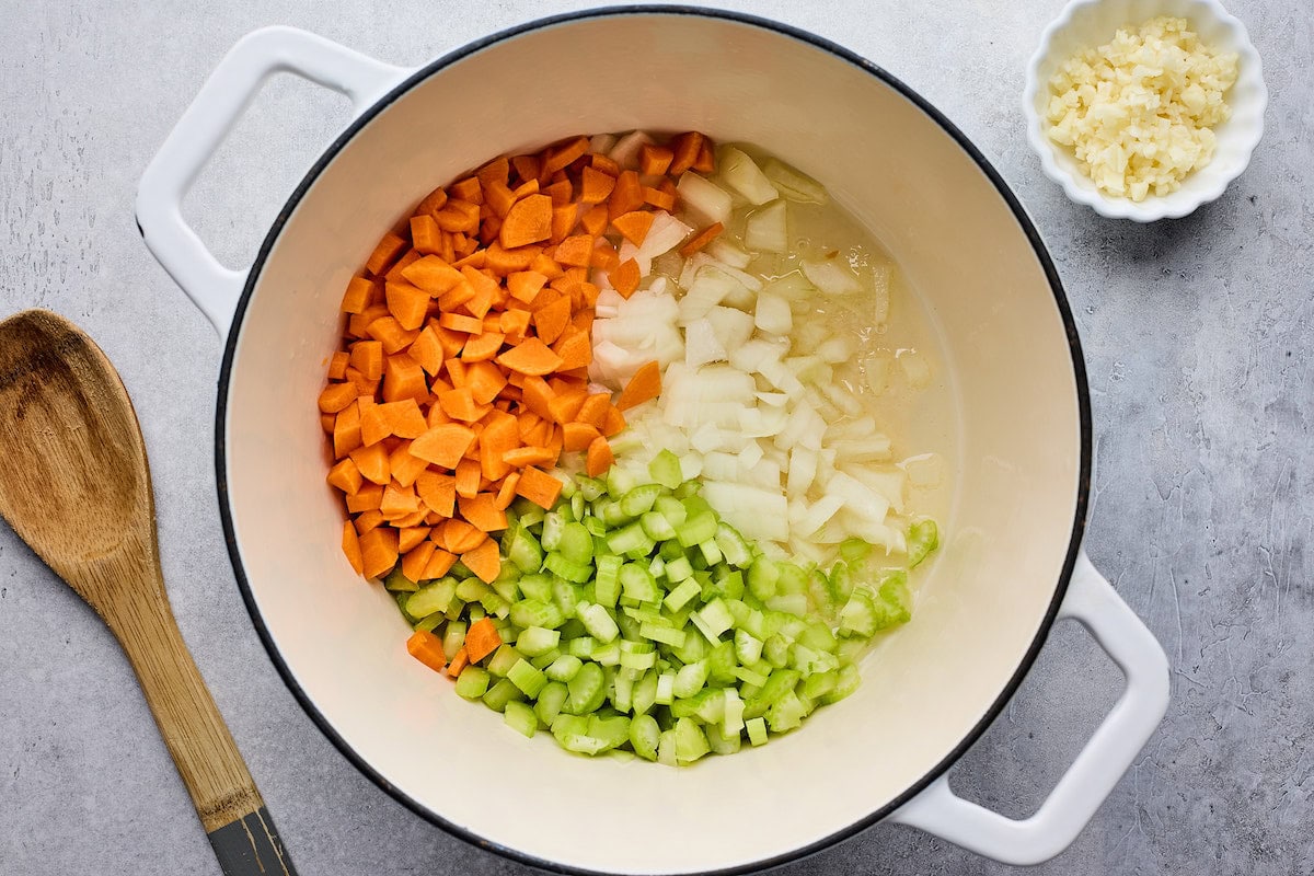 onion, carrot, and celery cooking in large white pot. 